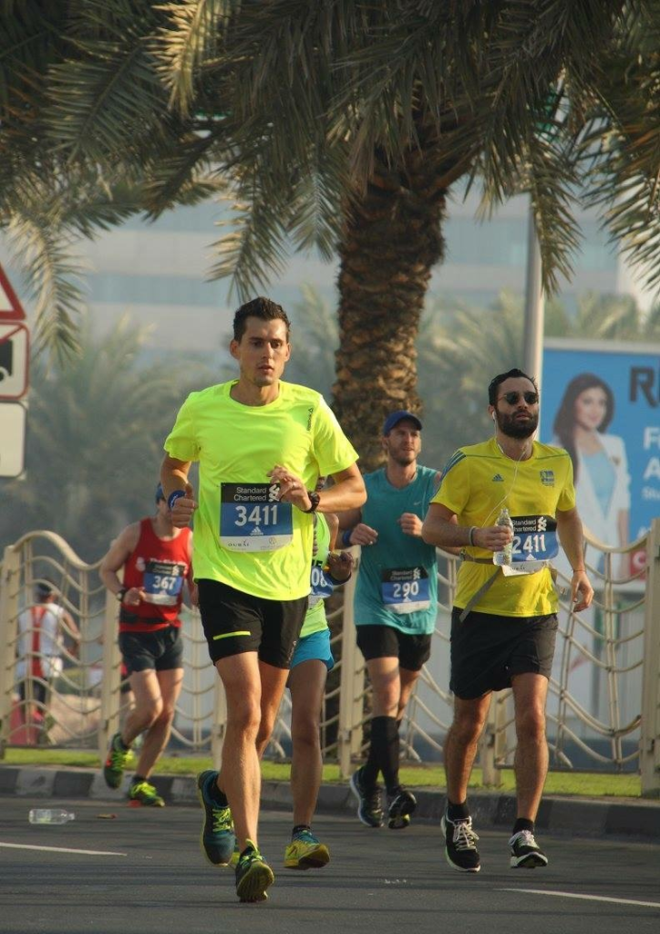 Coach Stef and runners in bright shirts with race bibs running outdoors along a palm tree-lined road