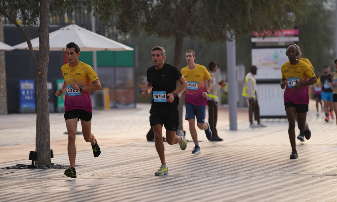 Coach Stef with a group of runners competing in a community running event, wearing race bibs, on a boardwalk