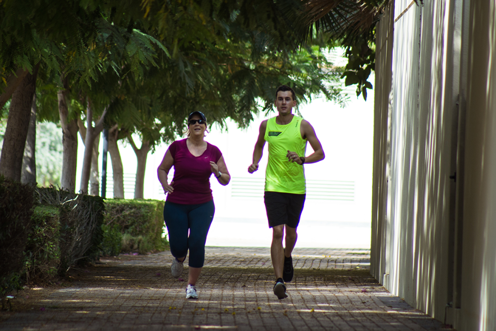 Coach Stef running along a tree-lined path with a community runner